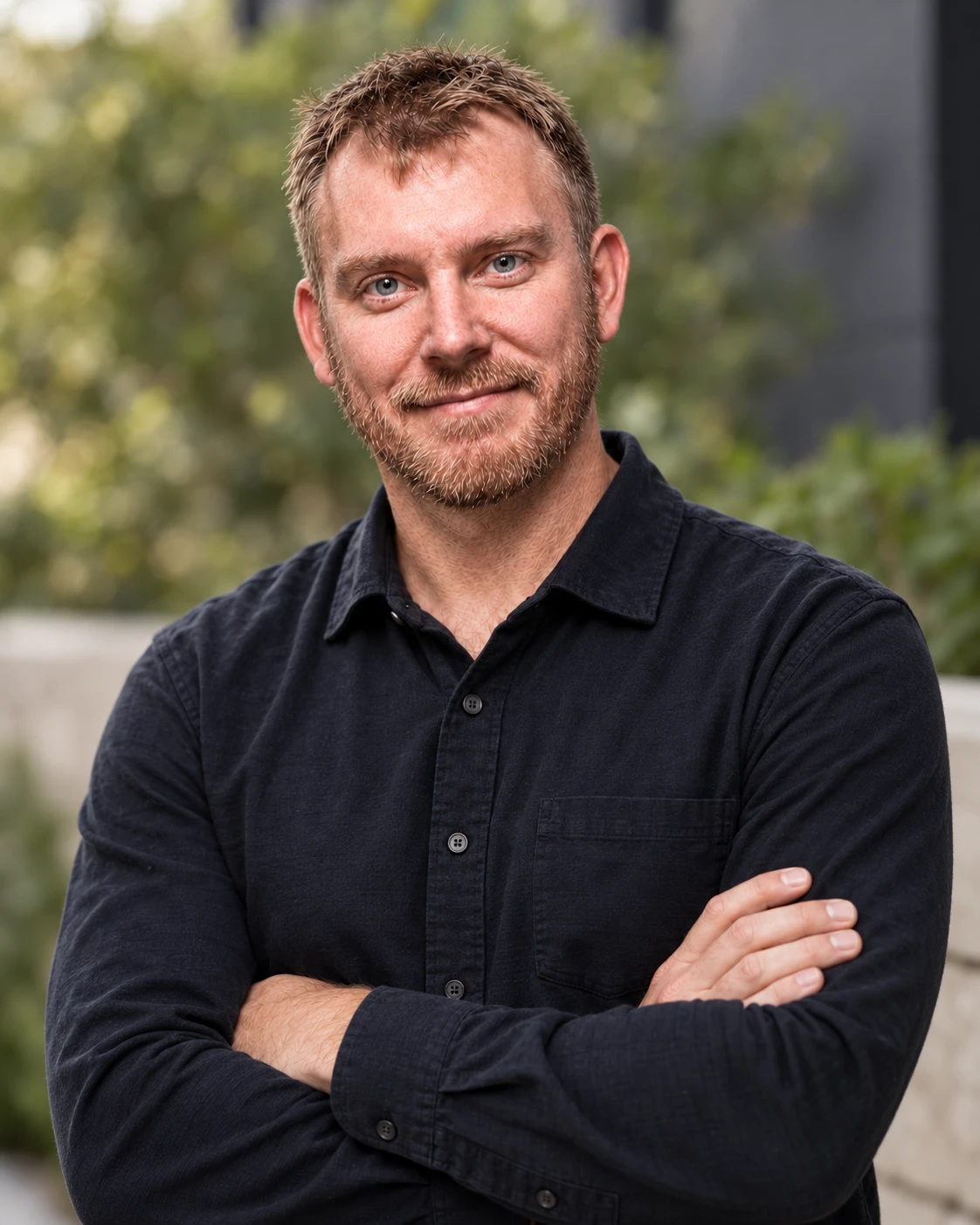 Micah Iverson outdoors, arms crossed, in a black button-up